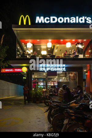 Mysore, India - October 27, 2013: Illuminated Mcdonalds Restaurant at night on intersection of JLB Road and Dhanavantri Road. Row of motorcycles and g Stock Photo