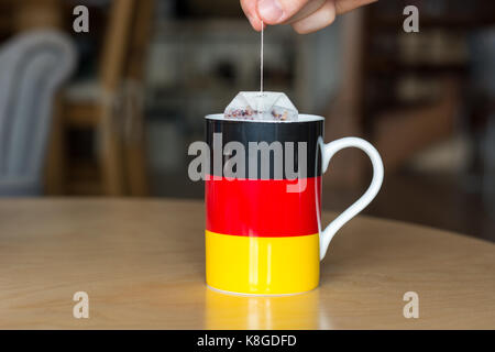 Putting a teabag in a mug with a German flag on it close up with blurry background Stock Photo