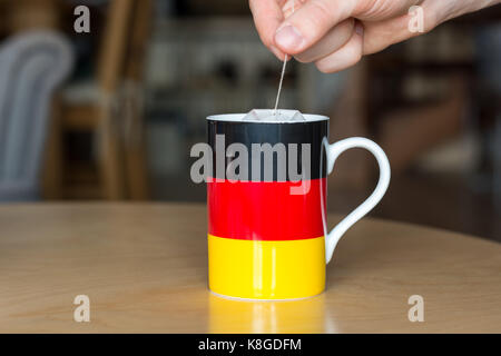 Putting a teabag in a mug with a German flag on it close up with blurry background Stock Photo
