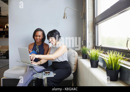 Two women sitting, working on laptop, on laptop stand Stock Photo