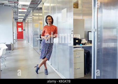 Portrait of businesswoman standing in office corridor, leaning against office surround, smiling Stock Photo