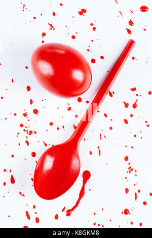 Overhead view of red painted easter egg and spoon with  splatters on white background Stock Photo