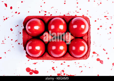 Overhead view of red painted easter eggs in carton with  splatters on white background