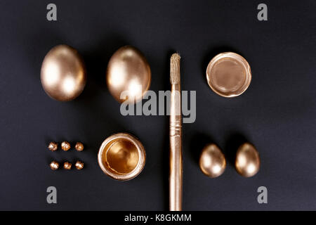Overhead view of gold painted easter eggs and paintbrush on black background Stock Photo