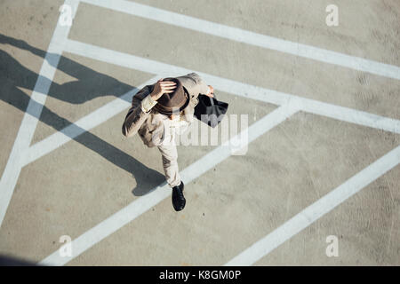 Young man walking across road, holding hat on head, overhead view Stock Photo
