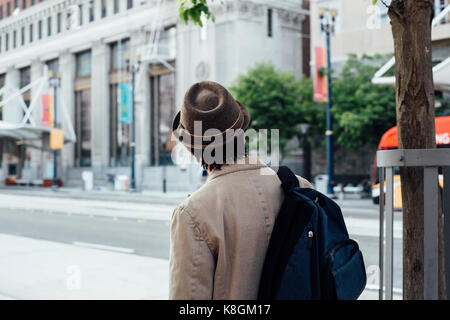 Young man walking outdoors, carrying backpack, rear view Stock Photo