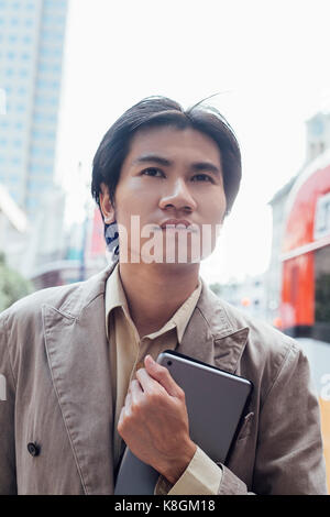 Young man walking outdoors, carrying digital tablet, close-up Stock Photo