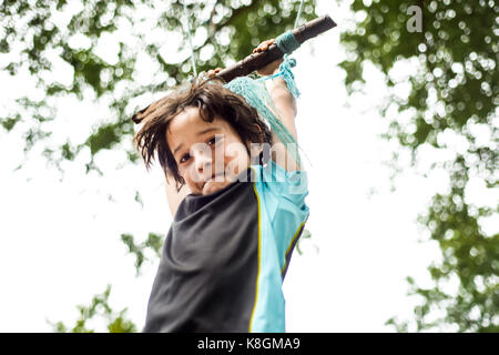 Young boy swinging on home-made swing in tree, low angle view Stock Photo