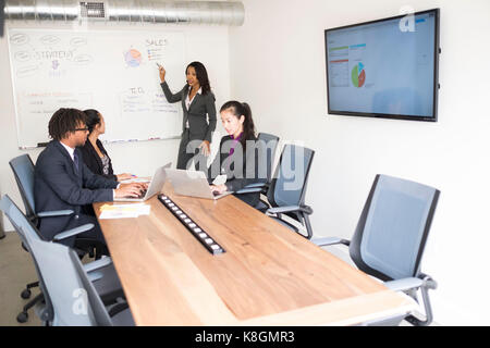 Businessman and businesswomen in meeting room, businesswoman, standing at front, explaining business strategy Stock Photo