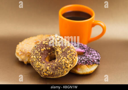 Delicious donuts with chocolate, coconut and pink glazed with some chips of chocolate, with an orange cup of coffee in a wooden background Stock Photo