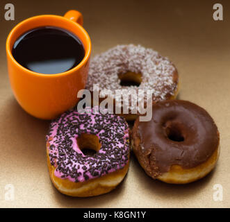Close up of a delicious donuts with chocolate, coconut and pink glazed with some chips of chocolate, with an orange cup of coffe in a wooden background, top view Stock Photo