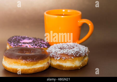 Delicious donuts with chocolate, coconut and pink glazed with some chips of chocolate, with an orange cup of coffe in a wooden background Stock Photo
