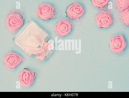 Perfume bottle with bow and pink roses on blue background. Vintage toning, copy space Stock Photo