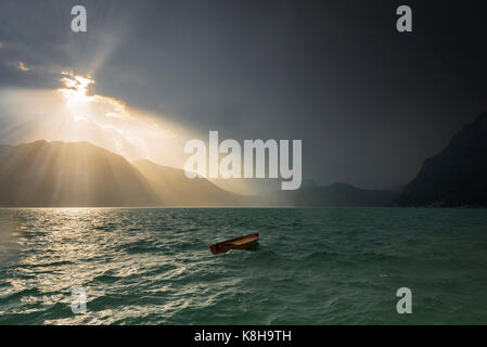 Thunderstorm raging on Lake Iseo with sun bursting through clouds and abandoned boat bopping up and down in the waves, Lombardy, Italy Stock Photo