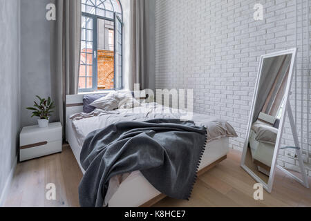 Loft bedroom with white brick wall, double bed and mirror Stock Photo