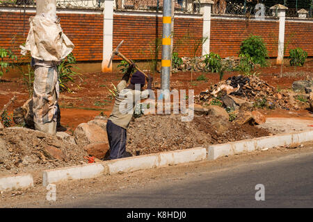 Construction worker digging hole with pickaxe by road, Nairobi, Kenya Stock Photo