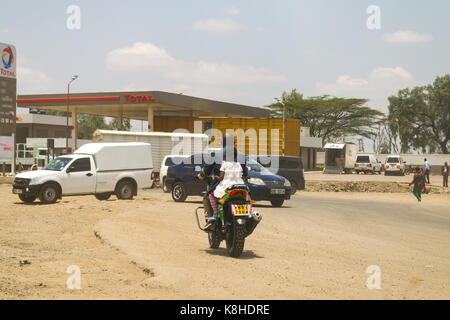 Little girl rides on the back of motorbike on busy road, Nairobi, Kenya Stock Photo