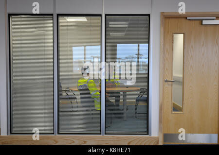 Tow construction workers or engineers talking in a modern glass fronted office building viewed from outside as if looking in spying and eavesdropping Stock Photo