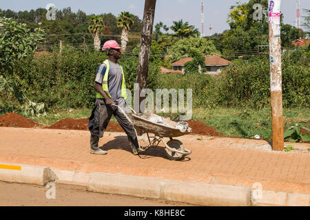 Construction worker walking pushing wheelbarrow on pavement, Nairobi, Kenya Stock Photo
