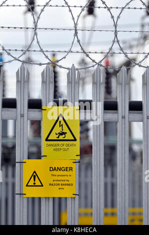 an electricity board sub station with palisade fencing and danger, danger of death yellow signs attached to the fencing as warnings to trespassers Stock Photo