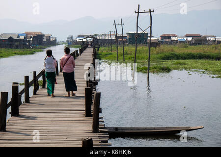 Burma, Myanmar: little girls, pupils viewed from behind walking on a footbridge in the village of Mang Thawk, Inle Lake Stock Photo