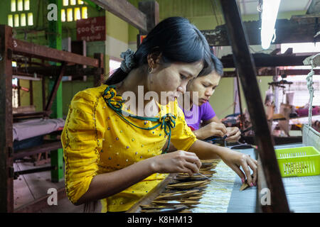 Burma, Myanmar, Mandalay: weaving workshop. Women working in front of a weaving loom: young women, weavers with Thanaka, a yellow beauty product, on t Stock Photo