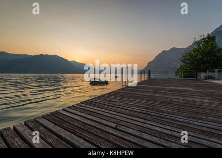 Jetty with wooden timber planks and boat ont he lake in the sunset over Lake Iseo and surrounding mountains, Lombary, Italy