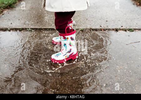 Low section of girl wearing rubber boots while standing in puddle Stock Photo