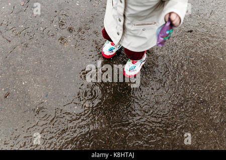 Low section of girl wearing rubber boots while standing on wet footpath Stock Photo