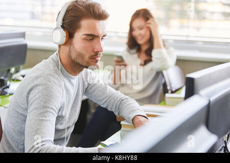 Student as programmer with computer wearing headphones in university Stock Photo