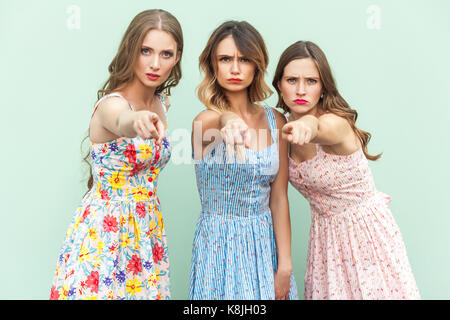 Hey you! Young adult womans, pointing fingers and looking at camera. On green background. Indoor, studio shot Stock Photo