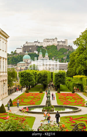Salzburg, Austria - July 4, 2013: Visitors are walking in beautiful Mirabell Gardens, a castle Hohensalzburg is seen on the background. Stock Photo