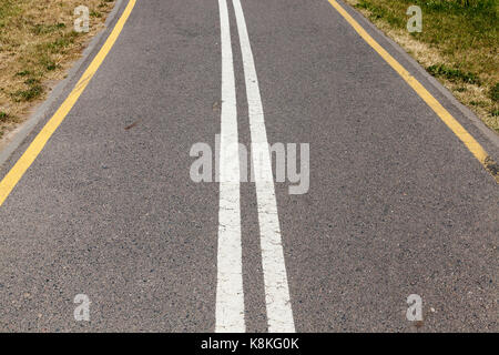 Asphalted road divided into two stripes by white lines. On the edge of the road yellow lines Stock Photo