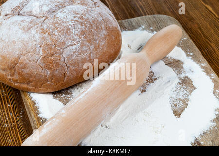 Baked rye bread, flour and rolling pin lying on a wooden board and prepared for baking new bread. Photo close-up at an angle Stock Photo