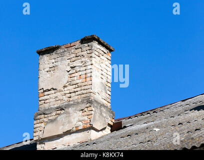 photo taken close-up of an old chimney made of brick, located on the roof of the house. Blue sky in the background Stock Photo