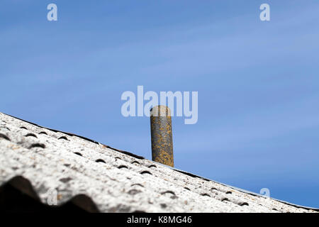 old chimney installed on the roof of a building covered with slate. Photo close-up on a background of blue sky. On the pipe grows lichen yellow Stock Photo