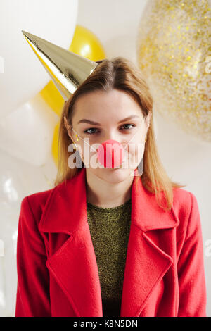 Young woman in a celebratory cap fooling around at a party on the background of falling confetti Stock Photo