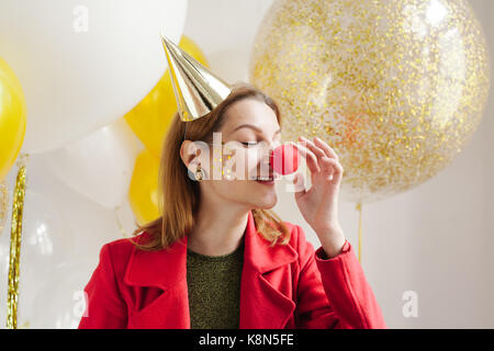 Young woman in a celebratory cap fooling around at a party on the background of falling confetti Stock Photo