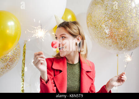 Young woman in a celebratory cap fooling around at a party on the background of falling confetti Stock Photo