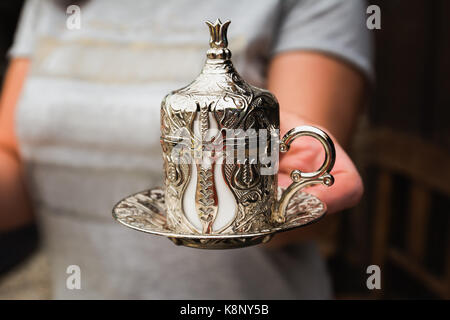 Woman is serving Turkish coffee in a traditional silver cup. Stock Photo