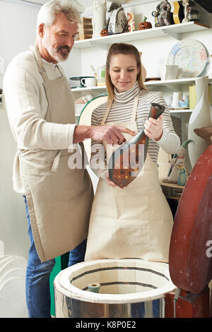 Tutor With Female Student In Pottery Studio Firing Vase In Kiln Stock Photo