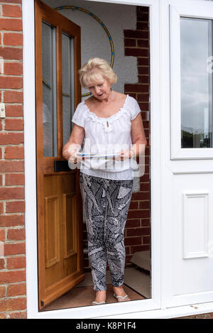 Woman standing at her front door reading her delivered mail Stock Photo