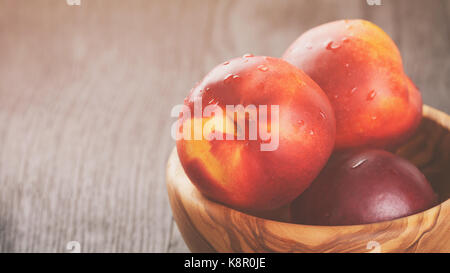 nectarines in olive wood bowl on oak table Stock Photo
