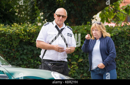 Parking warden writing out a parking ticket in the UK. Note: The lady shown is NOT the one receiving the ticket. Stock Photo