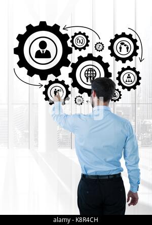 Digital composite of Business man interacting with people in cogs graphics against office background Stock Photo