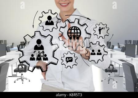 Digital composite of Business woman interacting with people in cogs graphics against office background Stock Photo