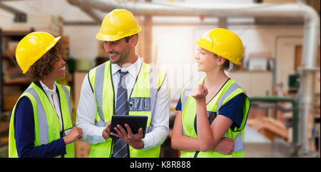 Architects in reflective clothing discussing over tablet computer against workshop Stock Photo