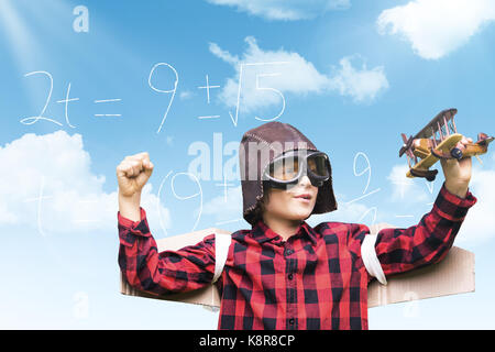 Boy in aviator cap holding toy airplane against blue sky Stock Photo