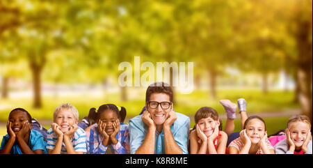 Portrait of teacher lying down with students against trees in grassy landscape Stock Photo