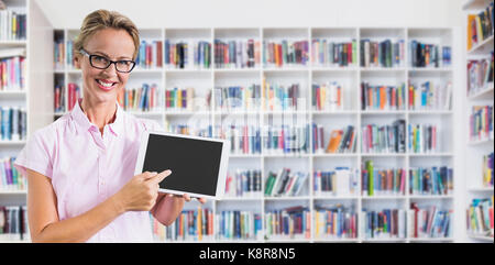 Portrait of smiling teacher holding digital tablet against teacher reading books to her students Stock Photo